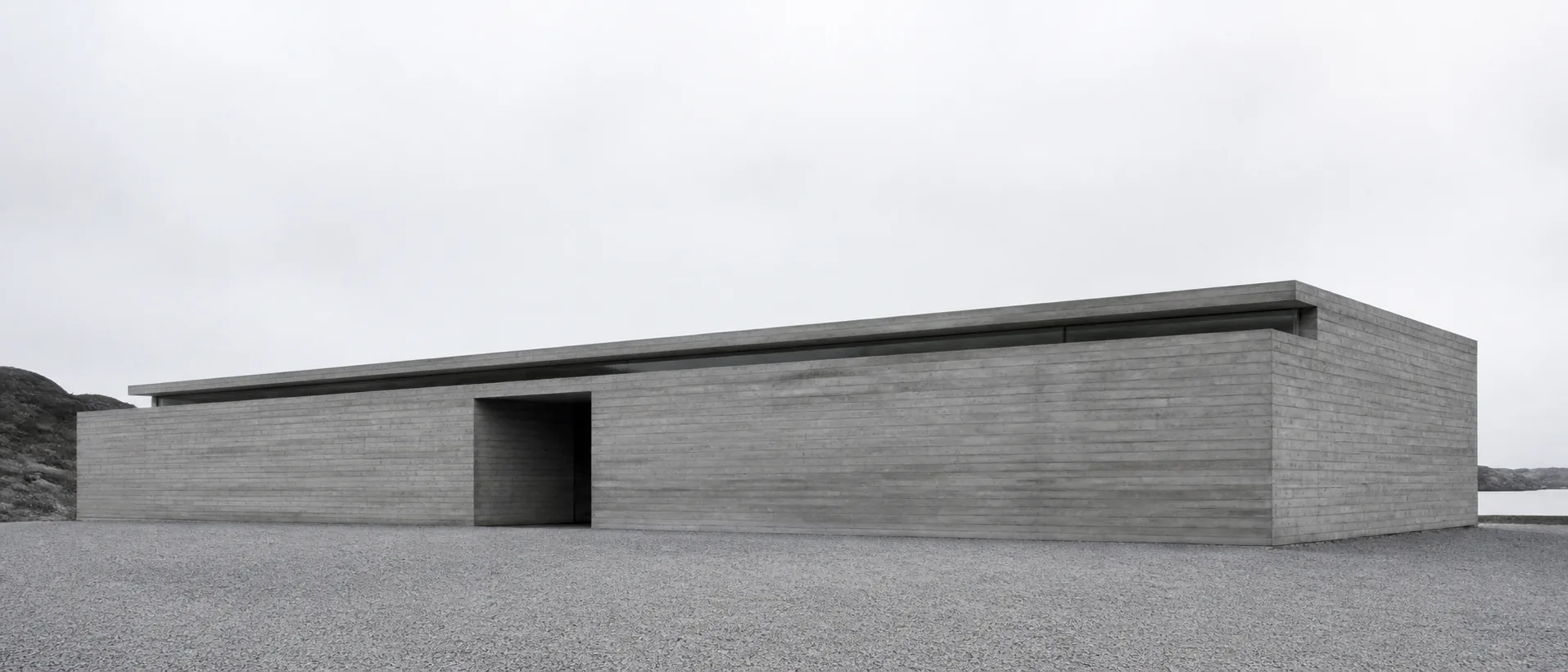 Long low concrete gallery opening onto a gravel forecourt.