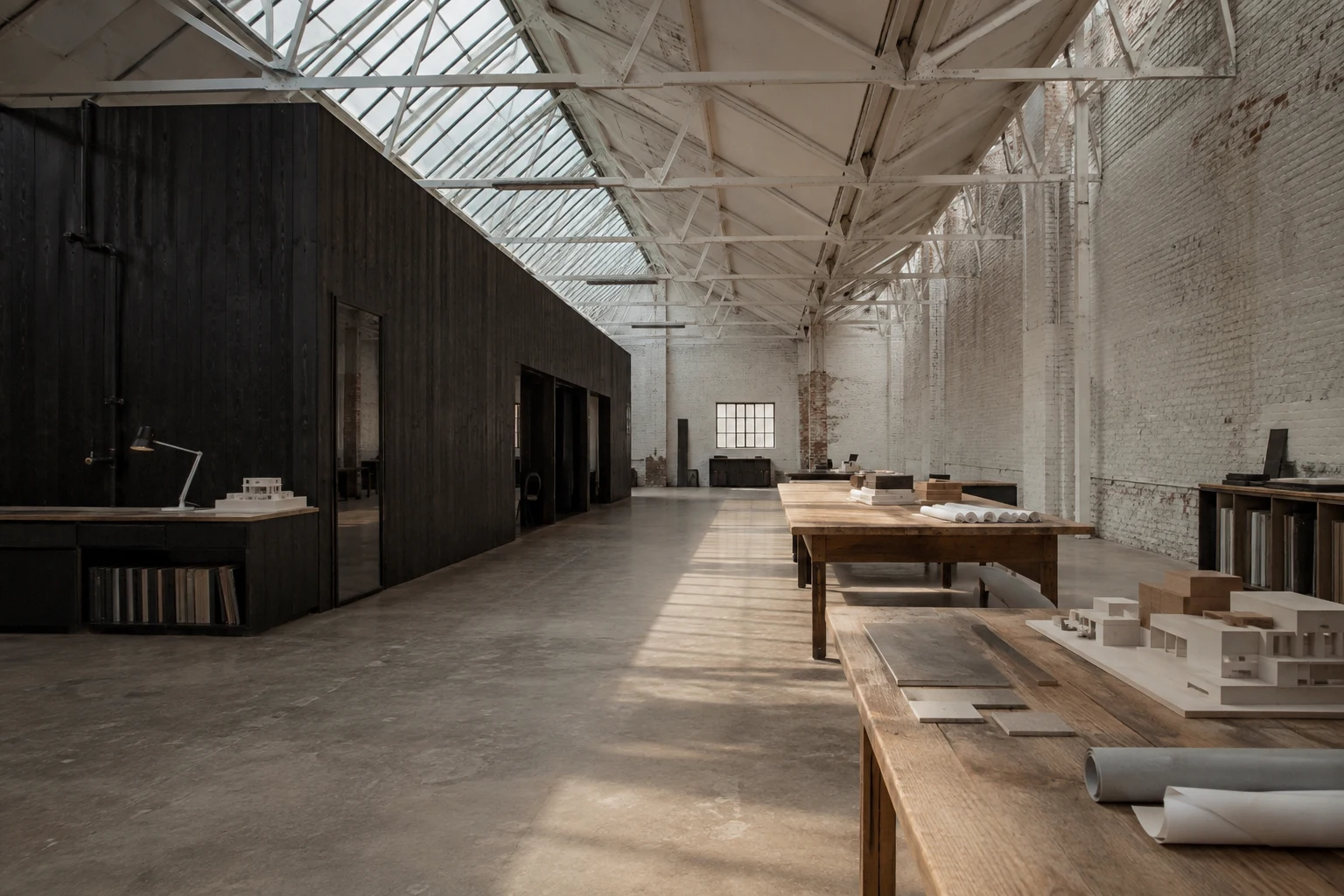 Daylight through steel trusses in a restored brick factory with timber worktables.